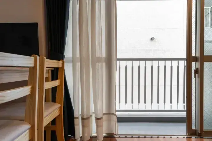 木製二段ベッドと白いカーテン、バルコニーが見える明るい部屋。