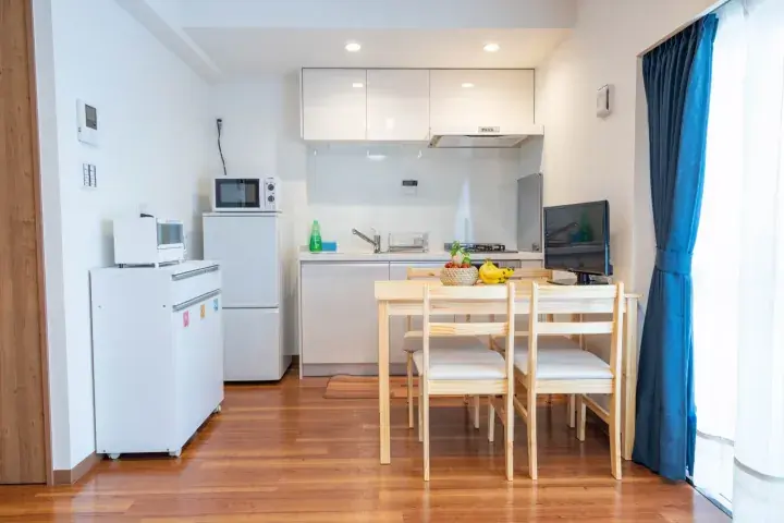 Modern open-plan kitchen and dining area with white cabinets, wooden flooring, and a blue curtain.
