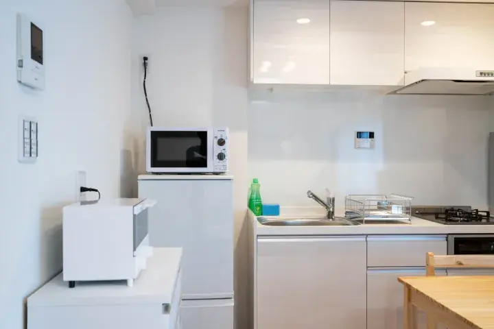 Modern white kitchen with microwave, sink, and wooden table in a Malaysian apartment.
