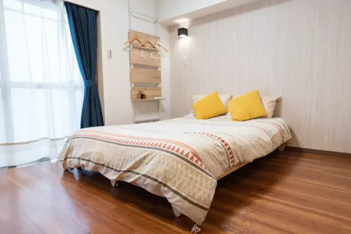 Bright bedroom with wooden flooring, a bed with yellow pillows, and a wall-mounted wooden coat rack.