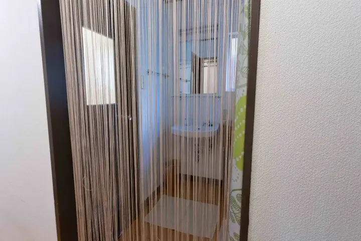 A beaded curtain doorway leads into a bright bathroom with a white sink and mirror.