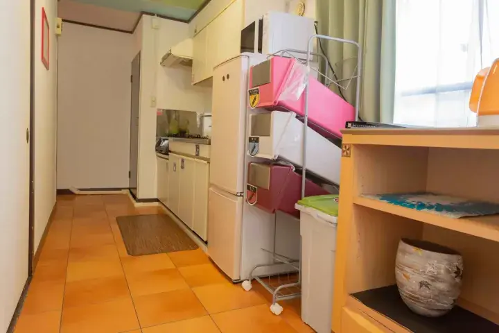 Compact kitchen area with white cabinets, a refrigerator, and a metal rack holding a pink item in a tiled room.