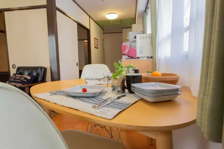 Modern dining table set with plates and cutlery in a bright apartment interior near a window with sheer curtains.