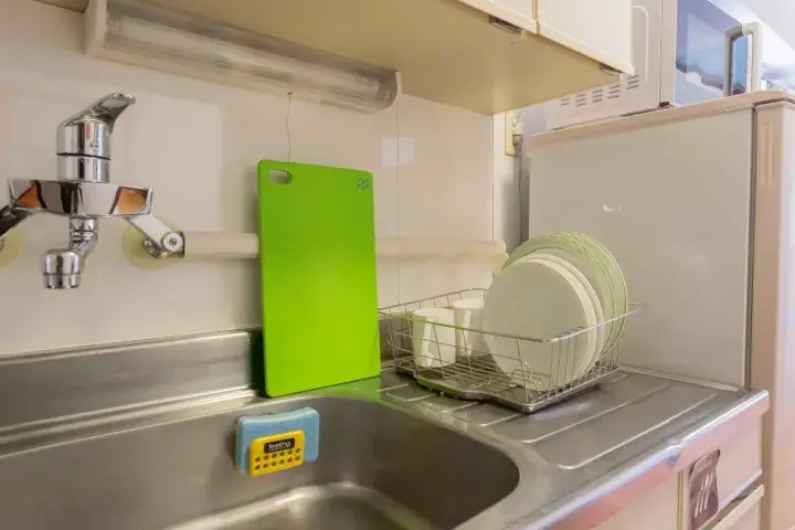 Modern kitchen sink with chrome faucet, green cutting board, and dish rack holding plates next to a refrigerator