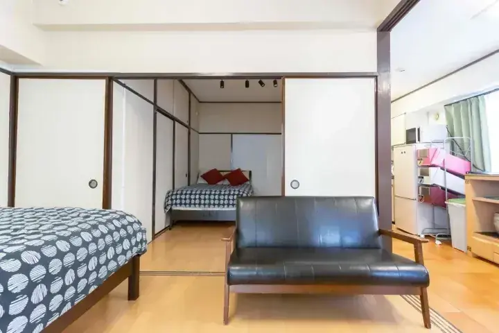 畳の部屋、布団、黒いレザーソファを備えたモダンな和風アパートメントのインテリア。
