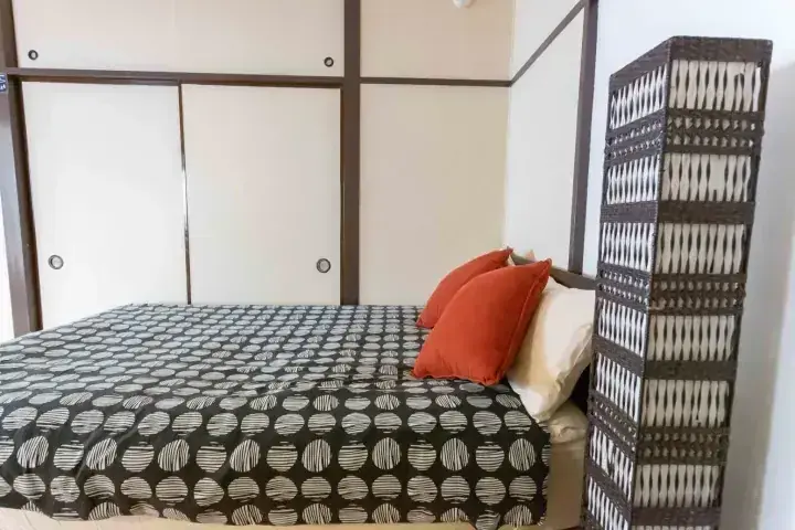 柄の寝具とオレンジ色の枕、和室のような部屋に設置された高さのある籐製仕切り棚。