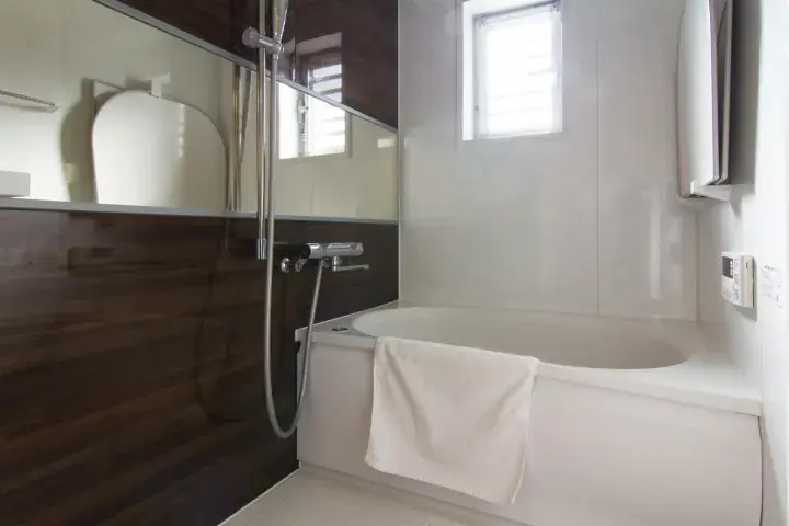 Modern bathroom with a white bathtub, dark wood paneling, and a shower fixture in a property setting.