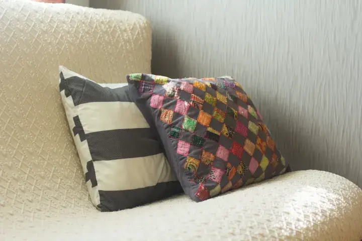 Two decorative cushions on a textured sofa, one with black and white stripes and another with a colorful patchwork design.