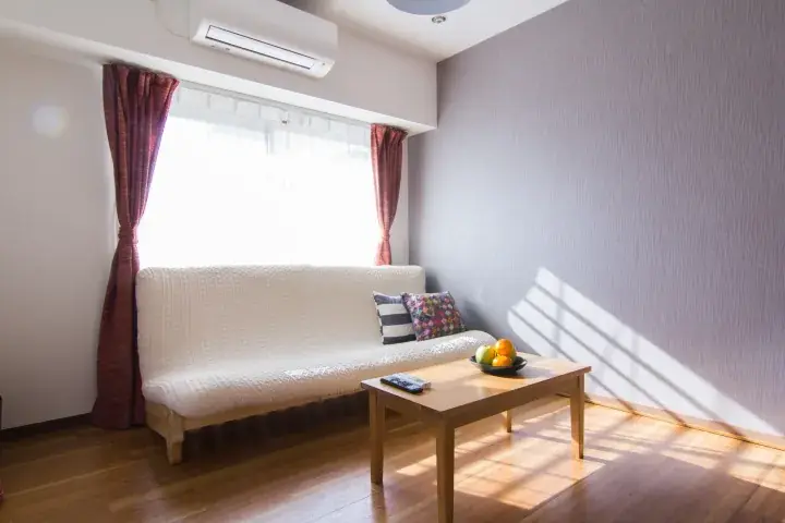 Bright living room with a white sofa, wooden coffee table, and sunlight streaming through the window.