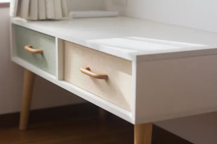 Modern white desk with wooden legs and two fabric drawers in pastel green and beige tones.