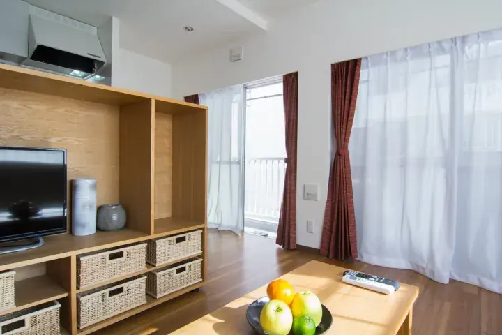 Bright living room with wooden TV unit, wicker baskets, and fruit bowl on coffee table near balcony.