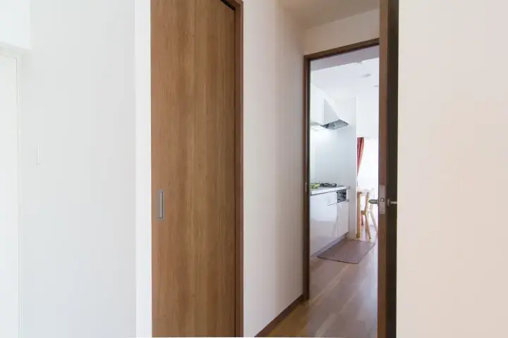 Modern wooden door leading to a bright kitchen with white cabinets and a range hood.