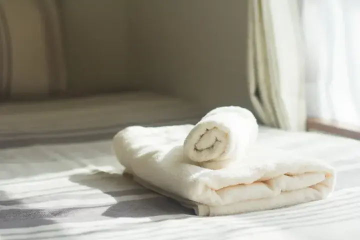 Neatly folded white towels on a sunlit bed with soft natural light filtering through sheer curtains.