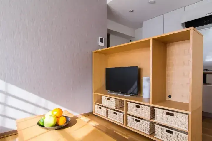 木製テレビ台と籐バスケット、テーブルの果物鉢が並ぶ日当たりの良いリビングルーム