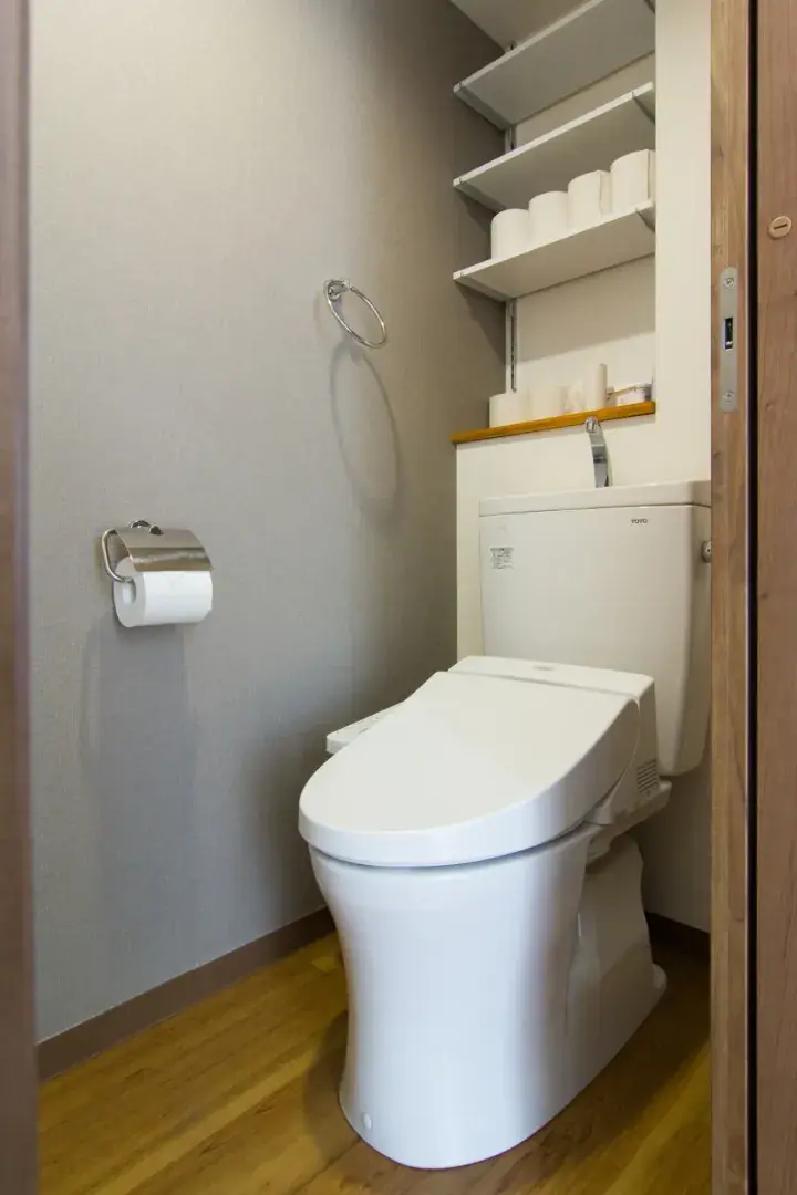 Modern white TOTO toilet with bidet seat in a compact bathroom featuring wooden flooring and wall-mounted shelves.