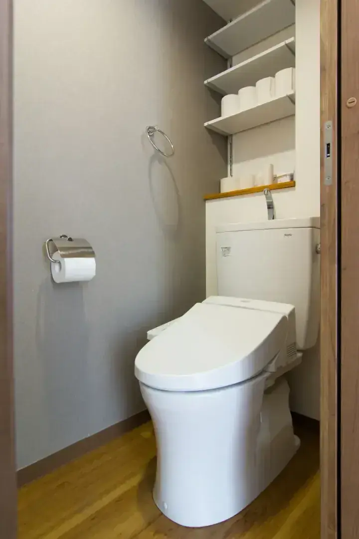 木製床と壁面収納棚を備えたコンパクトなトイレ。TOTO製温水洗浄便座付きの白いトイレ。