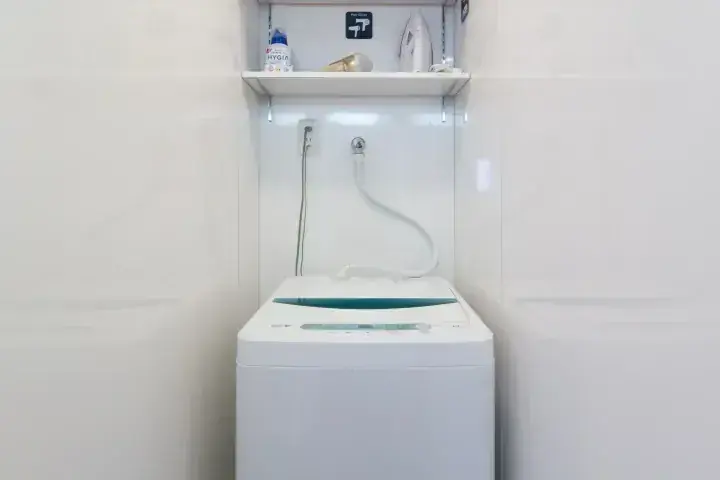 アイロンや洗剤が置かれた棚がある、清潔な洗濯スペースに設置された白い全自動洗濯機。