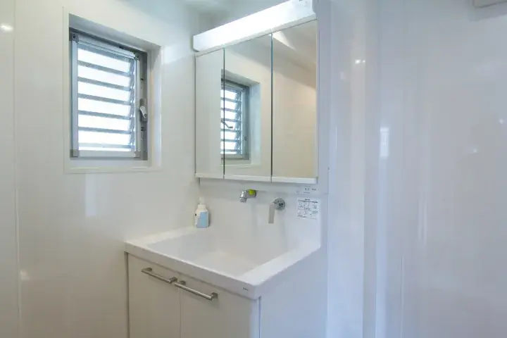 Modern white bathroom vanity with sink, mirrored cabinet, and window with louvers in a clean property interior.