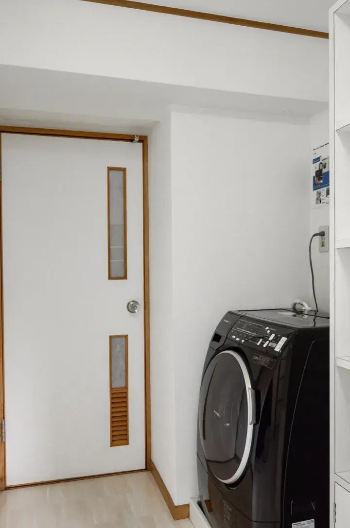 Modern laundry room with a black washing machine next to a white door with wooden frames and frosted glass panels.