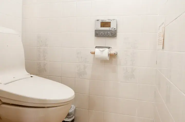 Modern white toilet with electronic bidet control panel mounted on tiled wall in a clean bathroom.
