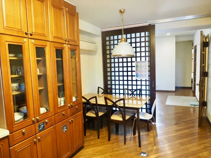 Warm wooden dining area with a glass-fronted cabinet, table, chairs, and a Japanese-style lattice screen.