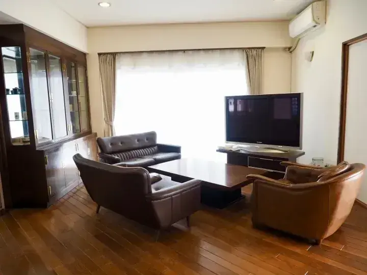 革張りのソファ、木製フローリング、大型テレビを備えた広々としたモダンなアパートのリビングルーム。