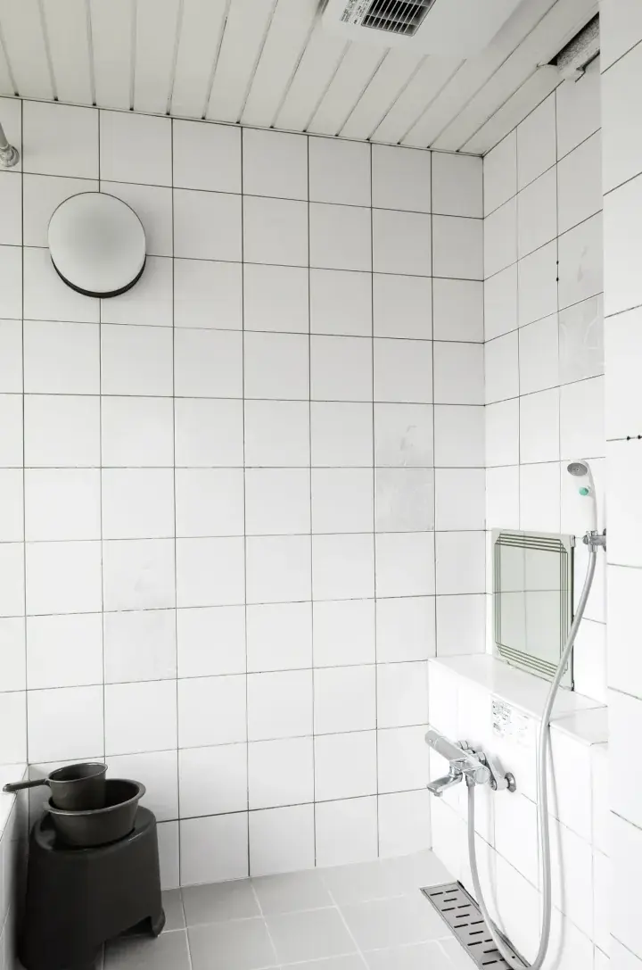 Modern bathroom interior with white square tiles, a round wall light, and a shower area with a handheld showerhead.