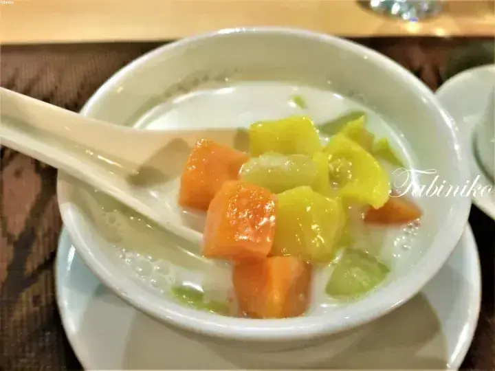 A bowl of tropical fruit dessert with papaya and mango in coconut milk, served with a spoon.