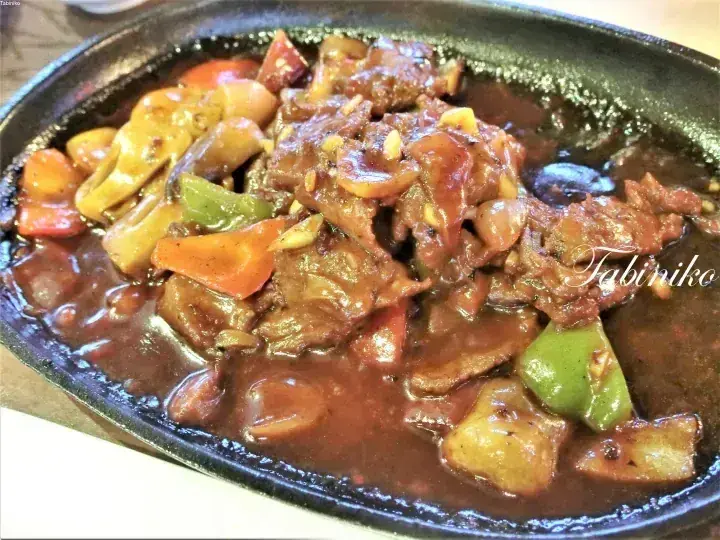 Sizzling beef and mushroom stir-fry with peppers and carrots served on a hot iron plate.