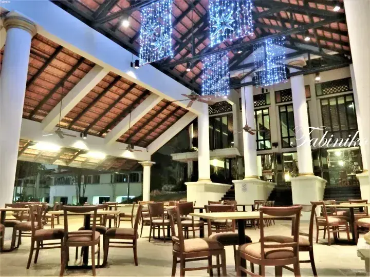 Spacious dining area with wooden tables and chairs under a high tiled roof adorned with blue star-shaped Christmas lights.