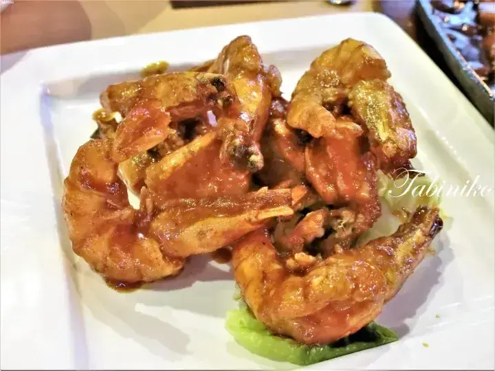 Glistening chili prawns served on a white rectangular plate with lettuce garnish.