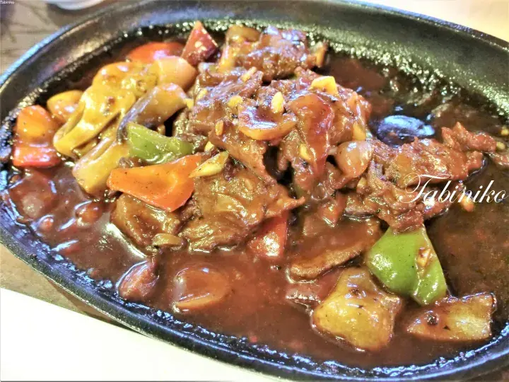 鉄板で提供される、ピーマンや人参を添えた牛肉とマッシュルームの炒め物。