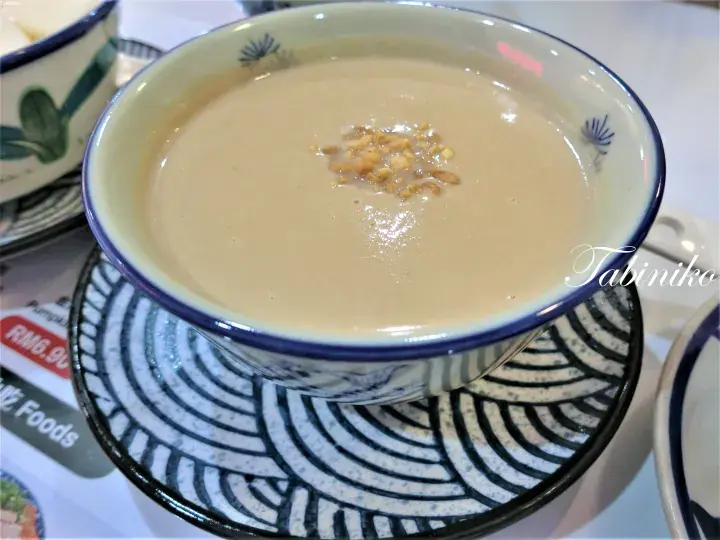 A bowl of creamy peanut soup topped with crushed peanuts, served in a blue-rimmed ceramic bowl on a patterned saucer.