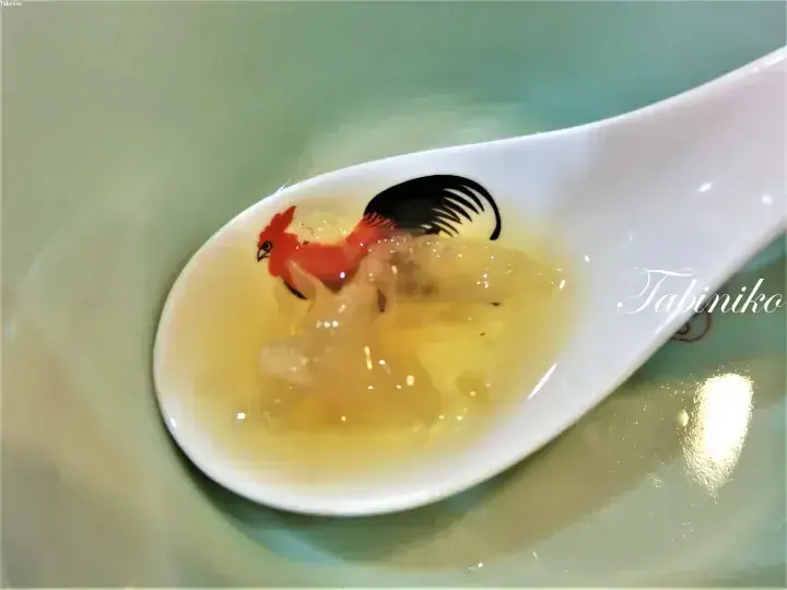 雄鶏のデザインが描かれた白い陶器のスプーンに盛られた、透明感のあるゼリー状の具材が入ったスープ。