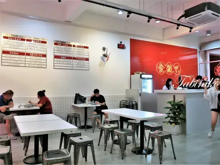 赤い壁の看板とメニューが並ぶ食堂barの店内で食事をする人々。