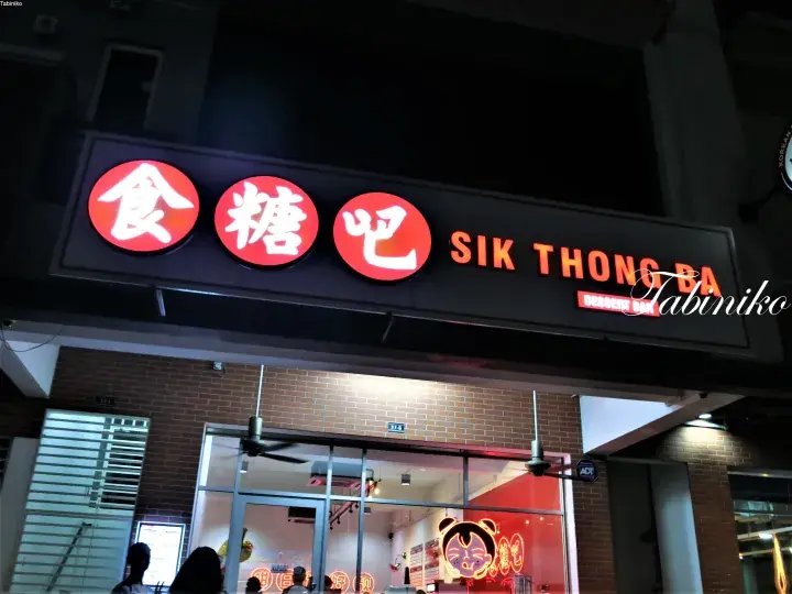 Sik Thong Ba storefront at night with illuminated red circular Chinese characters and orange English signage above the entrance.