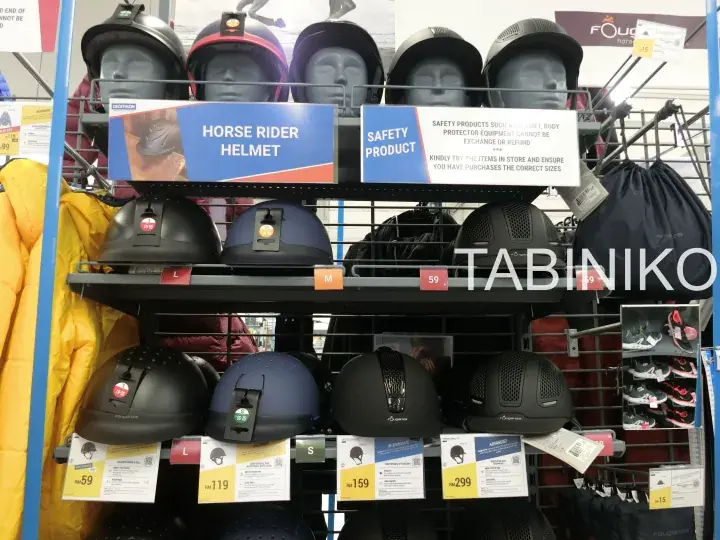Shelves of horse rider helmets and safety products displayed in a store with price tags and mannequin heads.