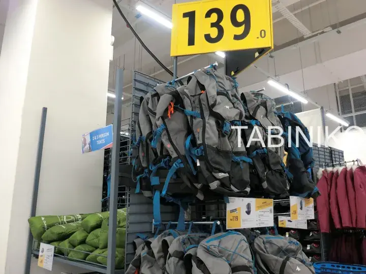 Grey and blue hiking backpacks hanging on a store rack with a yellow price tag showing 139.0