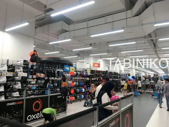 Shoppers browse the Oxelo sports section inside a Decathlon store, with the brand’s logo visible on the ceiling.