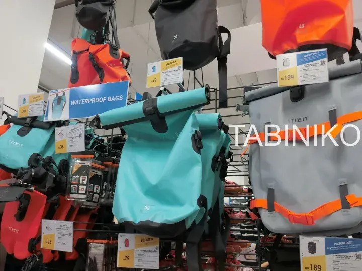 Colorful waterproof bags hanging on display racks with price tags in a store.
