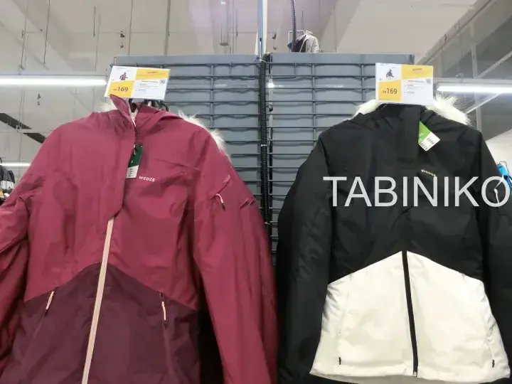 価格タグが付いた子供用の冬用ジャケット、1着はマルーン、もう1着は白と黒の配色でハンガーに掛けられている。