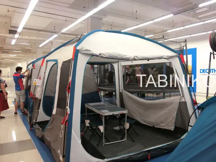 Large blue and white tent displayed indoors at Decathlon with a folding table and chairs set up inside.