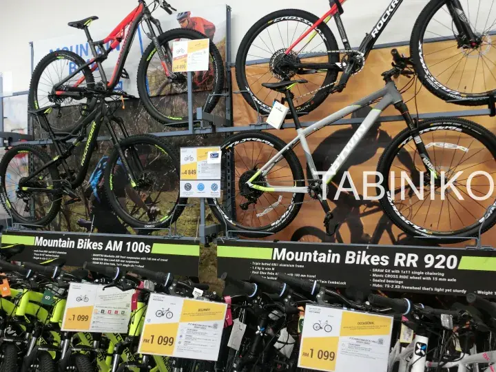 Mountain bikes AM 100s and RR 920 displayed on a rack at a bicycle shop with price tags.