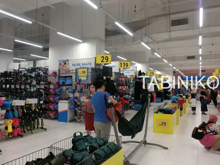 Interior view of a Decathlon store with customers browsing sports equipment and yellow price signs.