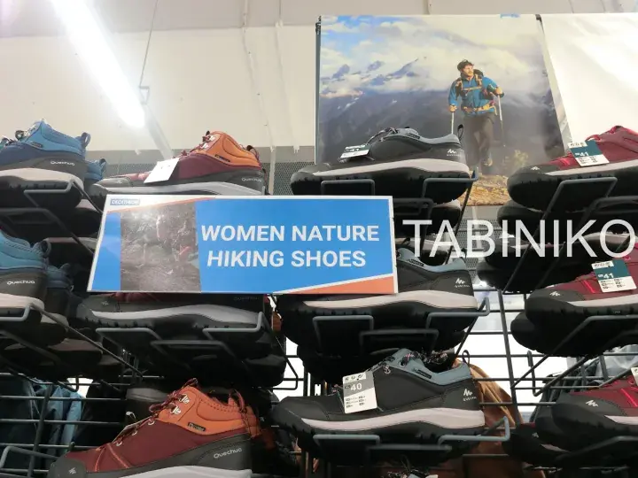 Display of Quechua women’s nature hiking shoes on a store rack with a blue sign.