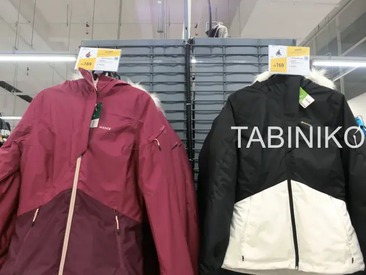 Two children’s winter jackets, one burgundy and one black with white, hanging on a rack with price tags.