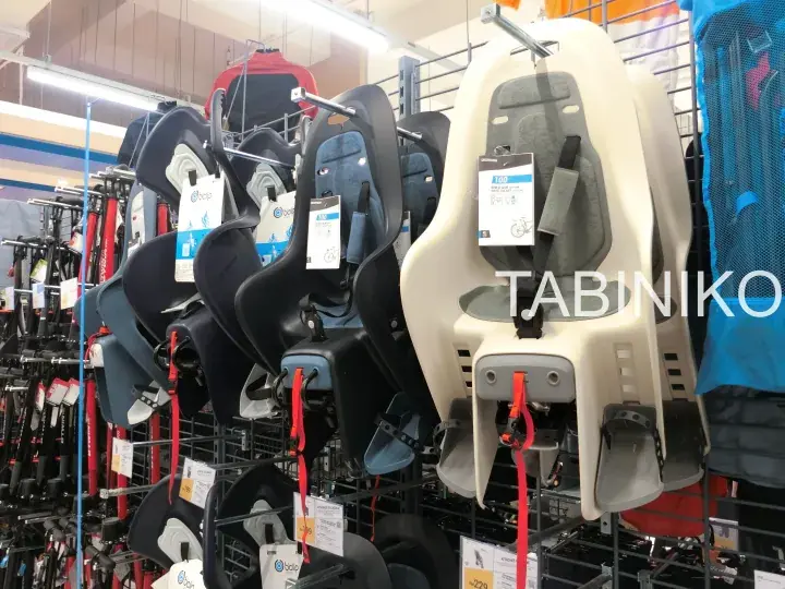 Various child bike seats displayed on a store rack, including black and cream models with safety straps.
