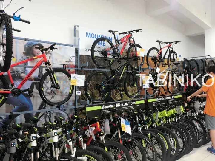 Mountain bikes displayed on racks in a Decathlon store, with signage for Mountain Bikes AM 100s and a customer browsing.