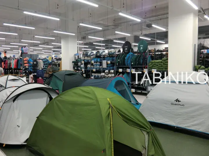 Quechua tents displayed in a Decathlon store aisle alongside camping gear and clothing.