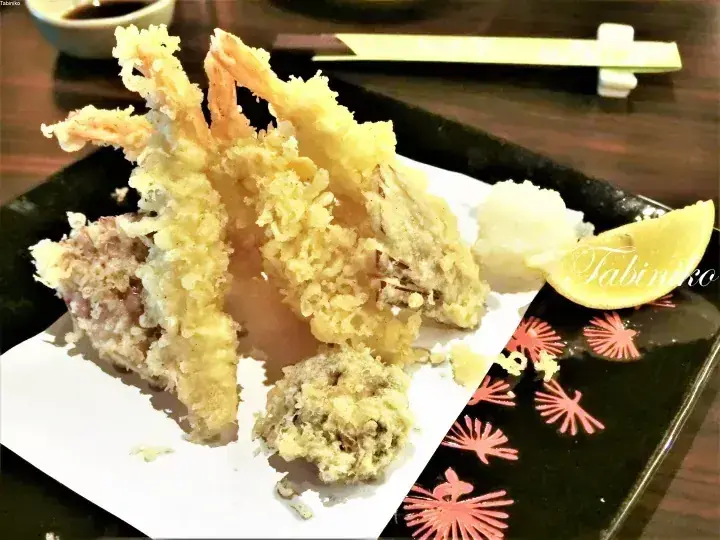 Crispy fried shrimp tempura served on a black plate with grated daikon radish and lemon wedge.